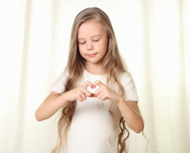küçük sarışın kız parmak tarafından yapılan kalp işareti gösterir