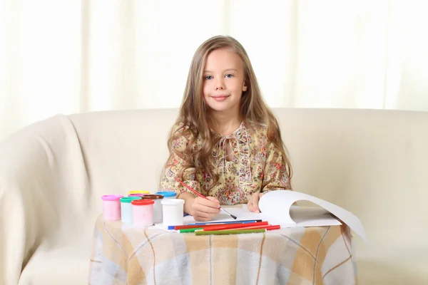 Blonďatá holčička kreslení doma na pohovce — Stock fotografie