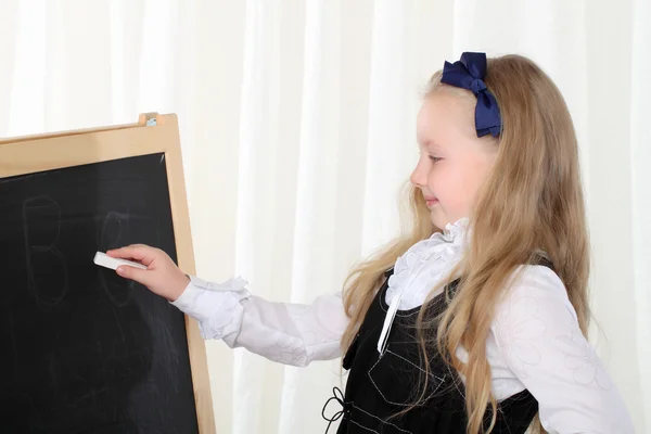 Klein meisje schrijven op zwarte bord met krijt — Stockfoto