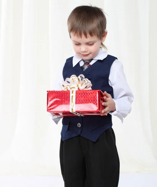 Pequeno menino inteligente em terno segurando redpresent caixa — Fotografia de Stock