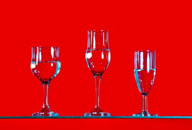 Düz bir zeminde çeşitli cam bardaklar güzel bir şekilde düzenlenmiştir, desen kırmızı bir arka plana sahiptir.