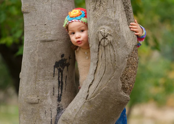 Słodki dziewczyna patrząc za drzewo kamień — Zdjęcie stockowe