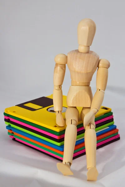 Artist's wooden manikin sitting on diskettes isolated — Stock Photo, Image
