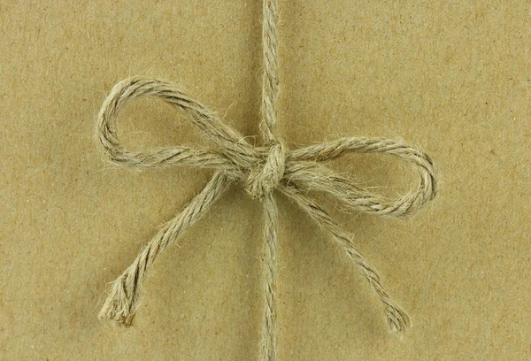 String tied in a bow, over brown recycled paper — Stock Photo, Image