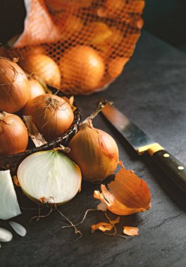 Kahverengi soğanlar ve tahta kesme tahtasındaki dilimler. Sağlıklı yemek arkaplanı. Bir sepette bir sürü soğan ve koyu renkli ve zarif dokusal arka planda bir sürü tabaklar..