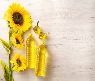 Beyaz arka planda beyaz ahşap masa üzerinde ayçiçeği yağı ile kompozisyon. Ayçiçeği yağlı plastik şişeler, taze sarı ayçiçekleri..