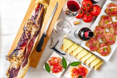 İspanyol mezeleri ve mezeler. Tapas ve aperatifler beyaz ahşap arka planda bir bardak şarap, olgun domates ve inek peyniri ile birlikte İber jambonu..