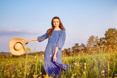 Mavi elbiseli kız tarlada yürüyor.