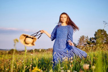 Mavi elbiseli kız tarlada yürüyor.