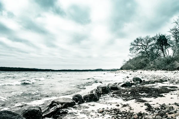 Ondas entrando em grandes rochas negras na costa em um dia frio — Fotografia de Stock