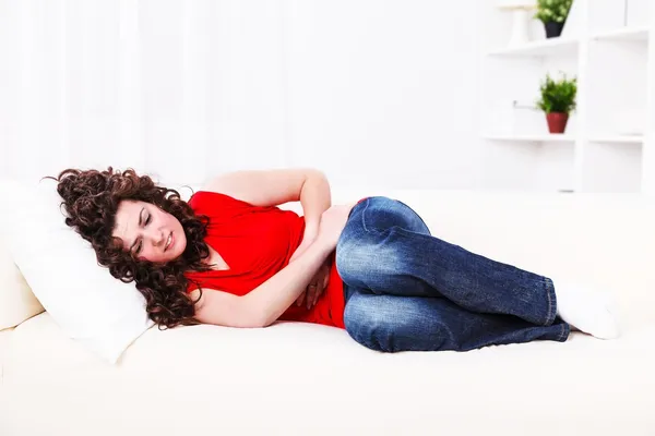 Mädchen auf dem Sofa mit Bauchschmerzen lizenzfreie Stockfotos