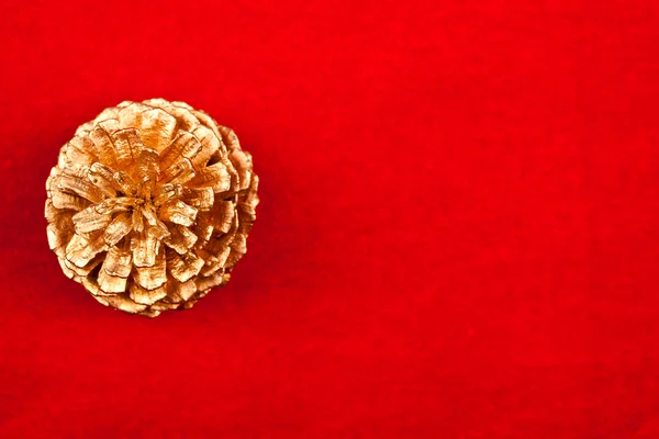 Cone de pinho dourado sobre fundo vermelho — Fotografia de Stock