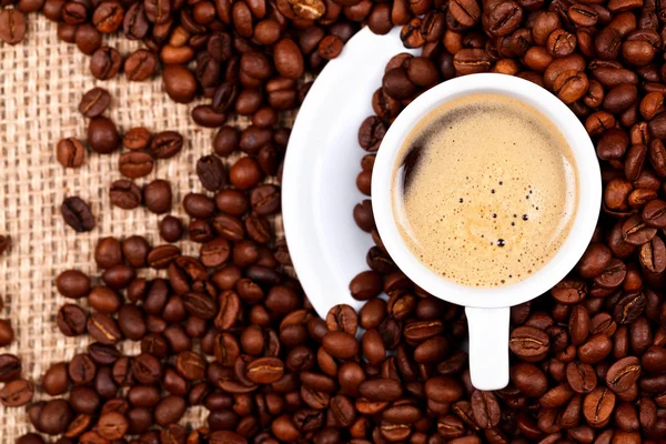 Xícara de café em grãos de café e serapilheira — Fotografia de Stock