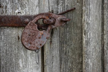 Eski paslı asma kilidin yakın görüntüsü eski gri ahşap bir kapı üzerinde.