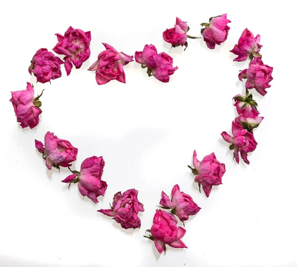 Wilted rose petals shaped into heart on white.