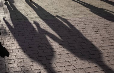 Kaldırım kenarındaki gölgeler Parlak güneş ışığı altında yürüyen iki insan.