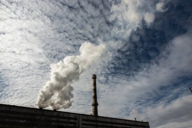 Beyaz ve gri duman ve buhar yüksek beton bir bacadan parlak mavi gökyüzüne karşı.