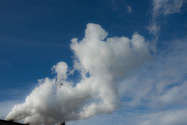 Beyaz ve gri duman ve buhar yüksek beton bir bacadan parlak mavi gökyüzüne karşı.