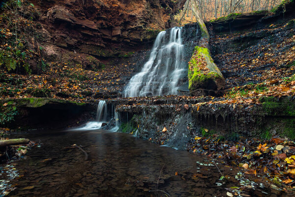 Tranquil waterfall scenery in the middle of autumn forest.