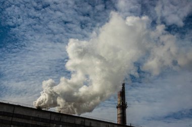 Beyaz ve gri duman ve buhar yüksek beton bir bacadan parlak mavi gökyüzüne karşı.