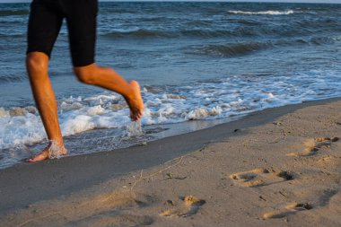kadın, deniz kumsalda önde koşuyor. bacaklar yakın çekim.