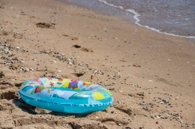 Çocuk renkli şişirilebilir yüzük ya da yüzer yaşam halkası ile kumsalda yüzer, kumsalda gün ışığı, deniz dalgası, kopyalanacak yer.