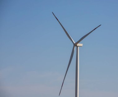 Rüzgar değirmeni ya da rüzgar türbini açık havada güneş ve mavi gökyüzü, koruma ve sürdürülebilir enerji kavramı ile elektrik üretmek için dönüşümlü olarak rüzgar tarlasında dönüyor..
