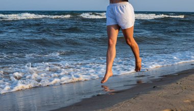 kadın, deniz kumsalda önde koşuyor. bacaklar yakın çekim.