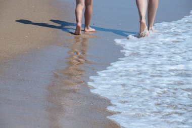 Ayaklar denizden sahile yürür. Deniz kıyısında. Kum dalgaları. Mutlu tatiller.