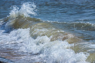 Deniz dalgaları kıyıdaki büyük kayalara çarpar ve büyük sıçramalar yaratır...