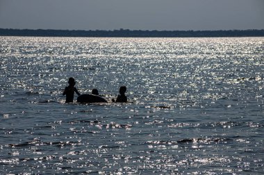 Sahilde güneşin altında yüzen çocukların siluetleri..