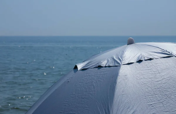 青い海の背景を背景に 前景に淡いピンクの縞模様のビーチ傘 — ストック写真