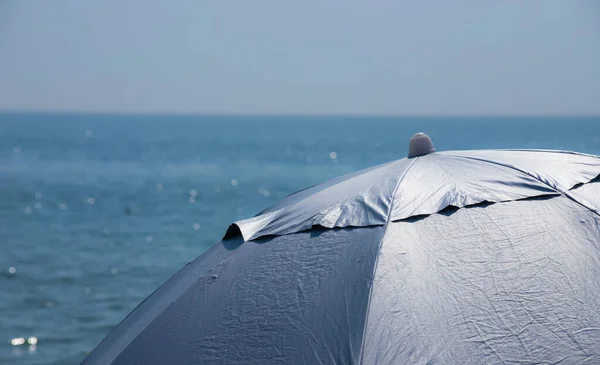 青い海の背景を背景に 前景に淡いピンクの縞模様のビーチ傘 — ストック写真