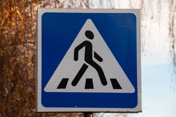 Traffic indicating sign, a blue crosswalk sign for pedestrians crossing the street or road on blur green trees and blue sky background in the city. No people. Selective focus.