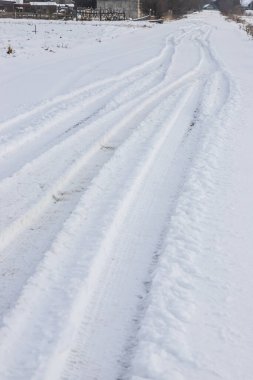 Çam ormanına giden bir tarlada karlı bir yol. Güneşli bir günde kış yolu, karla kaplı yeni araba pisti. Uzak kırsal kesimde derin bir kar tabakasında araba izleri var..