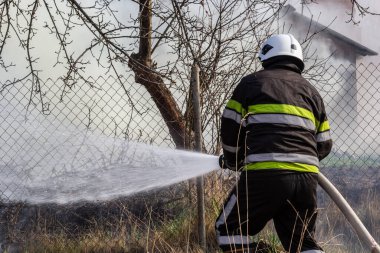 İlkbahar yangını, kırsal alandaki binaların yakınındaki kuru çimenleri yakmak. İtfaiyeci alevi söndürür. Çevre felaketi.