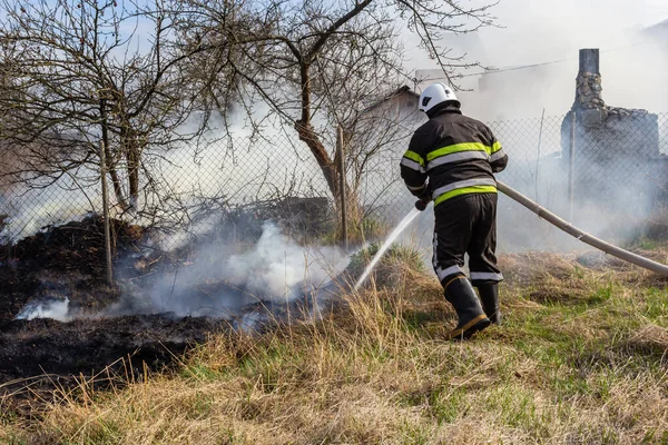 spring fire, burning dry grass near buildings in the countryside. Firefighter extinguishes the flame. Environmental disaster.