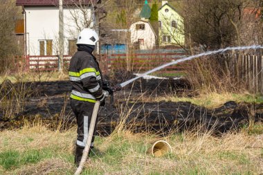 İlkbahar yangını, kırsal alandaki binaların yakınındaki kuru çimenleri yakmak. İtfaiyeci alevi söndürür. Çevre felaketi.
