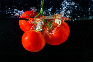 Suya düşen taze kırmızı domates. Su sıçraması ve siyah arka planda izole edilmiş hava kabarcıkları..