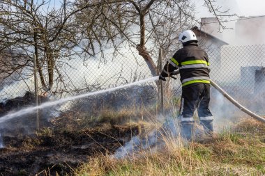 İlkbahar yangını, kırsal alandaki binaların yakınındaki kuru çimenleri yakmak. İtfaiyeci alevi söndürür. Çevre felaketi.