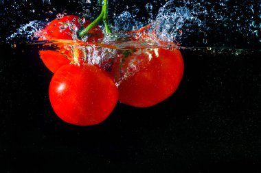 Suya düşen taze kırmızı domates. Su sıçraması ve siyah arka planda izole edilmiş hava kabarcıkları..