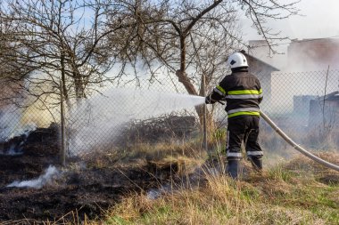 İlkbahar yangını, kırsal alandaki binaların yakınındaki kuru çimenleri yakmak. İtfaiyeci alevi söndürür. Çevre felaketi.
