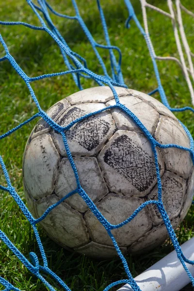 old soccer ball in the net on the background of grass soccer field. Summer sunny day.