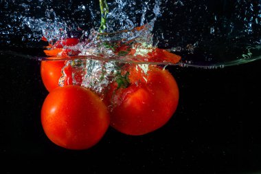 Suya düşen taze kırmızı domates. Su sıçraması ve siyah arka planda izole edilmiş hava kabarcıkları..