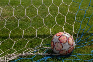 Çim futbol sahasının arka planında ağda eski bir futbol topu. Yaz güneşli bir gün.