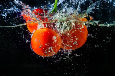 Suya düşen taze kırmızı domates. Su sıçraması ve siyah arka planda izole edilmiş hava kabarcıkları..