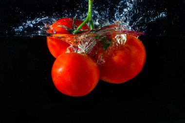 Suya düşen taze kırmızı domates. Su sıçraması ve siyah arka planda izole edilmiş hava kabarcıkları..
