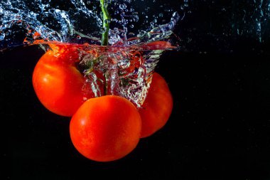 Suya düşen taze kırmızı domates. Su sıçraması ve siyah arka planda izole edilmiş hava kabarcıkları..