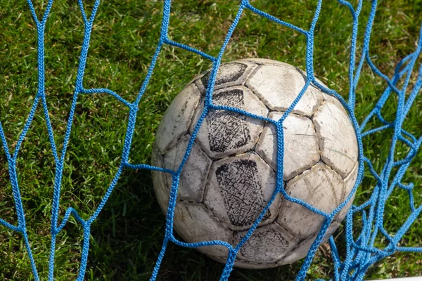 old soccer ball in the net on the background of grass soccer field. Summer sunny day.