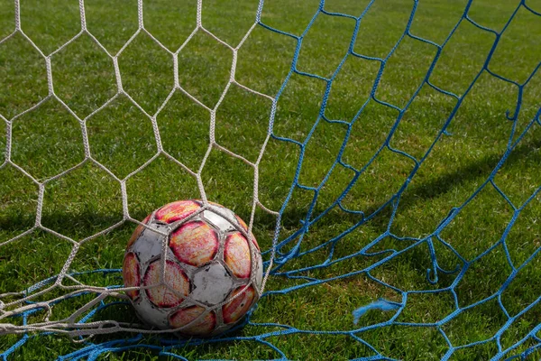 old soccer ball in the net on the background of grass soccer field. Summer sunny day.